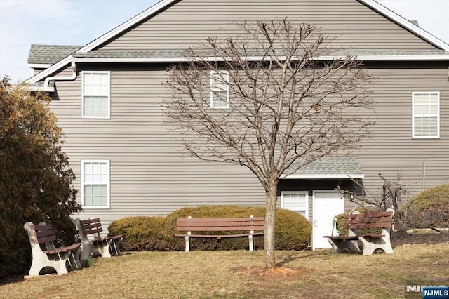 view of property exterior with a shingled roof and a lawn