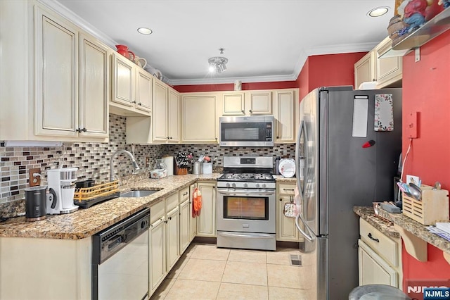 kitchen with light tile patterned floors, cream cabinets, a sink, appliances with stainless steel finishes, and decorative backsplash