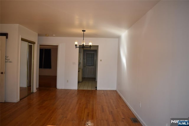 spare room featuring a chandelier, wood finished floors, and baseboards