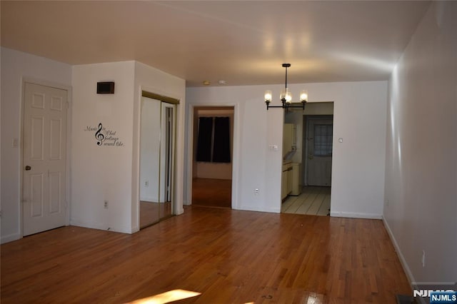 empty room with a chandelier, light wood-style flooring, and baseboards