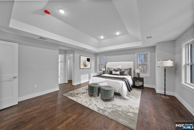 bedroom with a tray ceiling, recessed lighting, visible vents, wood finished floors, and baseboards