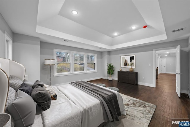 bedroom with a tray ceiling, dark wood finished floors, recessed lighting, visible vents, and baseboards