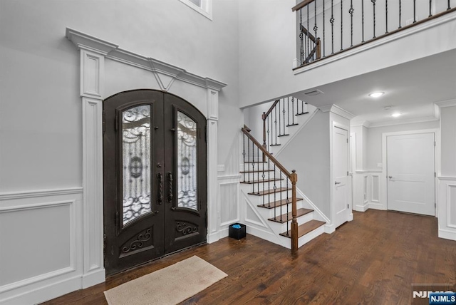 foyer entrance with stairway, ornamental molding, wood finished floors, french doors, and a decorative wall