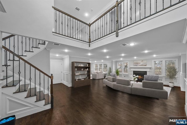 living room with a warm lit fireplace, visible vents, and ornamental molding