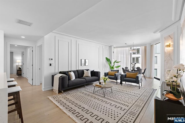 living room with light wood-type flooring, visible vents, and a decorative wall