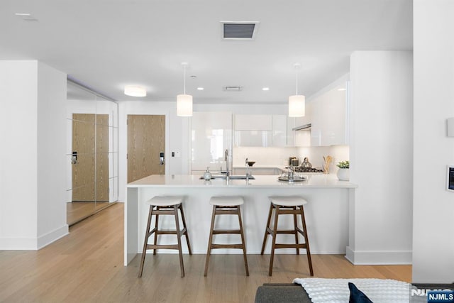 kitchen with a peninsula, a sink, visible vents, white cabinetry, and light countertops