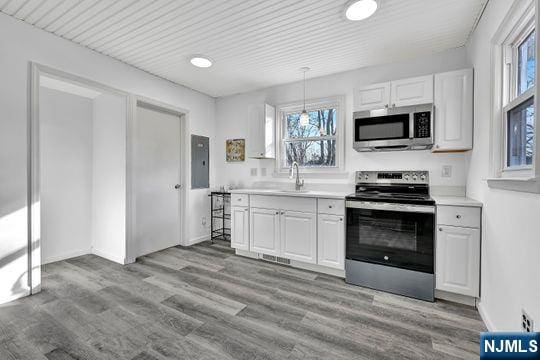 kitchen featuring stainless steel appliances, light countertops, white cabinets, a sink, and wood finished floors