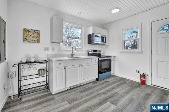 kitchen with appliances with stainless steel finishes, a sink, light wood-style flooring, and white cabinets