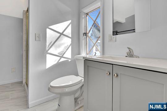 bathroom featuring toilet, an enclosed shower, vanity, and baseboards