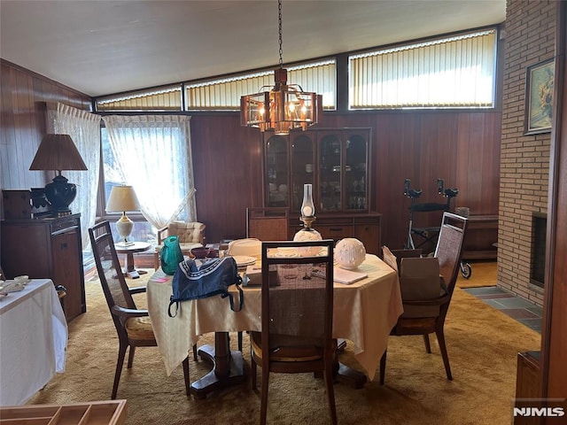 carpeted dining room featuring vaulted ceiling, wooden walls, a brick fireplace, and an inviting chandelier