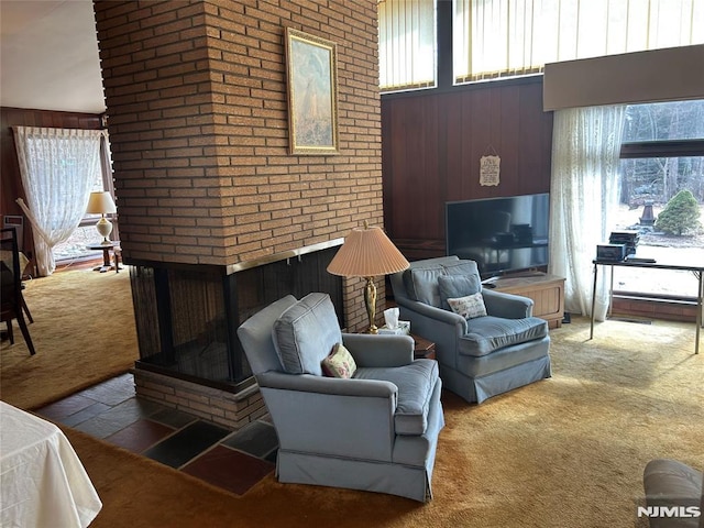 living area with a wealth of natural light, carpet flooring, wood walls, and a high ceiling