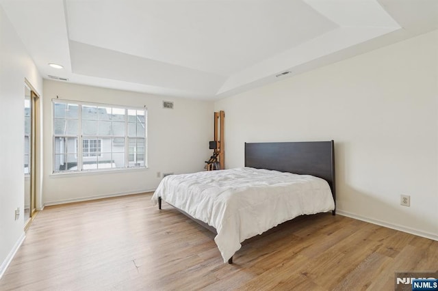 bedroom with light wood-style flooring, visible vents, and a raised ceiling