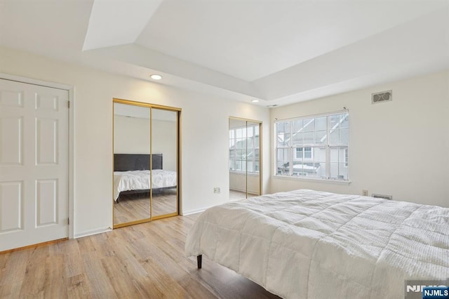 bedroom with recessed lighting, wood finished floors, visible vents, multiple closets, and a tray ceiling