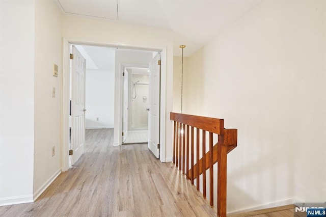 hall featuring light wood-style flooring, baseboards, and an upstairs landing