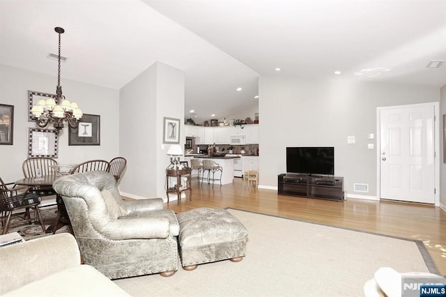 living room featuring lofted ceiling, visible vents, light wood-style flooring, and an inviting chandelier