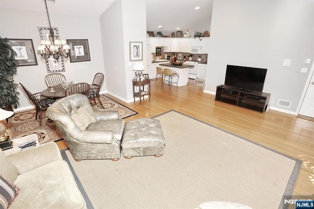 living area featuring light wood finished floors, baseboards, visible vents, and an inviting chandelier