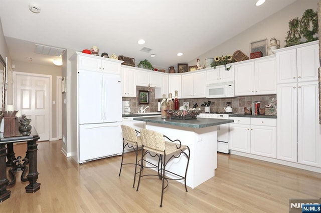 kitchen with lofted ceiling, dark countertops, a kitchen island, white appliances, and a kitchen bar