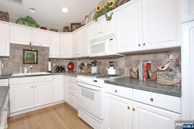 kitchen with white appliances, a sink, light wood-style floors, tasteful backsplash, and dark countertops