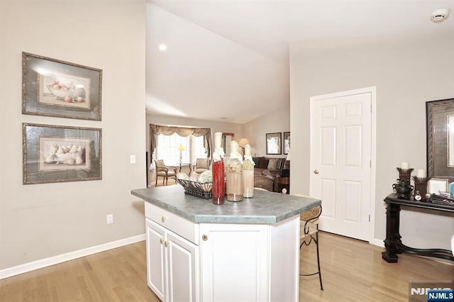 kitchen featuring vaulted ceiling, light wood-style floors, white cabinetry, and a center island