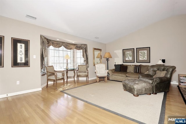 living room with visible vents, vaulted ceiling, baseboards, and wood finished floors