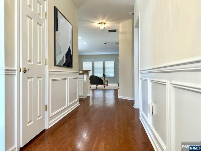 hall featuring dark wood-style floors, a wainscoted wall, visible vents, and a decorative wall