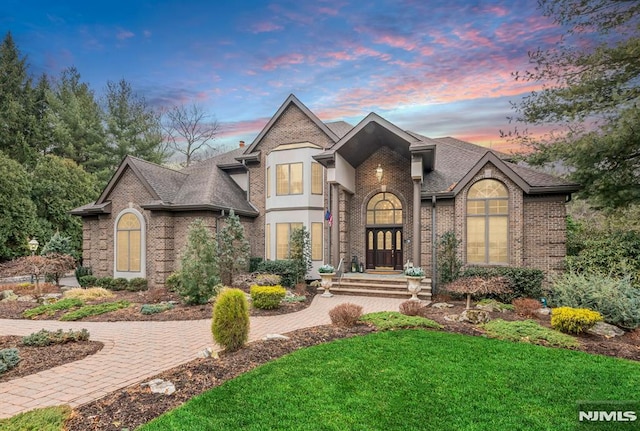 french provincial home featuring brick siding, a front lawn, and roof with shingles