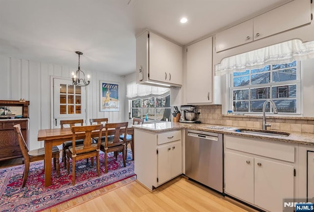 kitchen featuring a sink, light wood-style floors, white cabinets, stainless steel dishwasher, and backsplash