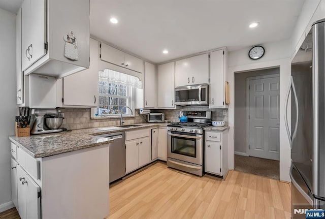 kitchen featuring stainless steel appliances, light wood-style floors, a sink, and decorative backsplash