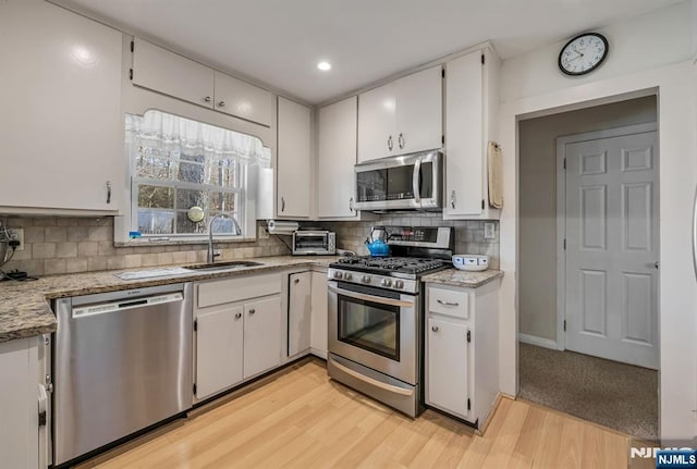 kitchen featuring backsplash, appliances with stainless steel finishes, white cabinets, and a sink