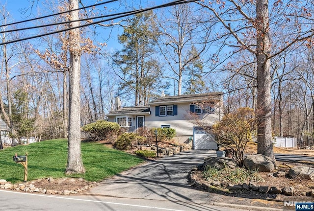 tri-level home with an attached garage, a chimney, aphalt driveway, and a front yard