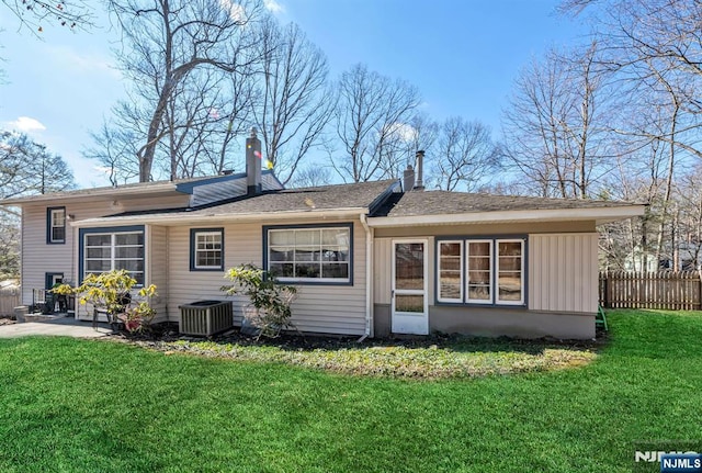 back of property with central air condition unit, fence, a lawn, board and batten siding, and a chimney