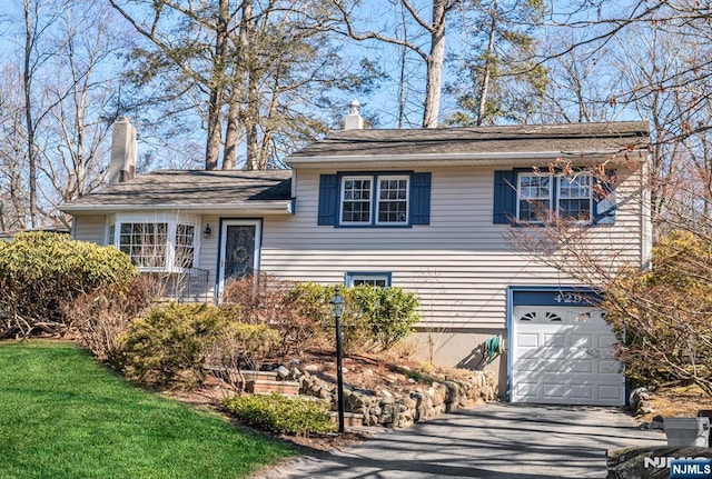 split level home featuring a garage, driveway, a chimney, and a front yard