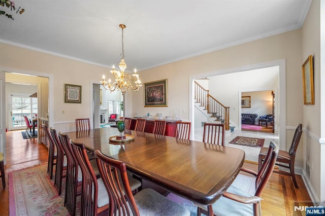 dining space featuring light wood-style floors, stairway, a chandelier, and crown molding