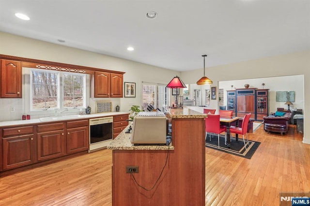 kitchen featuring dishwashing machine, a center island, hanging light fixtures, light wood-style floors, and a sink