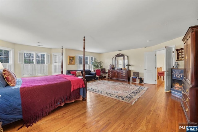 bedroom featuring a lit fireplace and light wood-style flooring