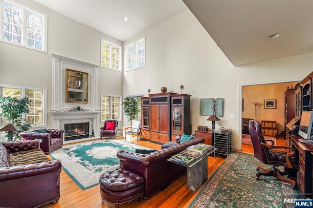 living area with a towering ceiling, a wealth of natural light, wood finished floors, and a high end fireplace