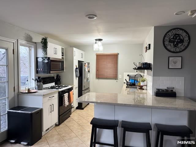 kitchen with a peninsula, a kitchen bar, white cabinetry, and stainless steel appliances