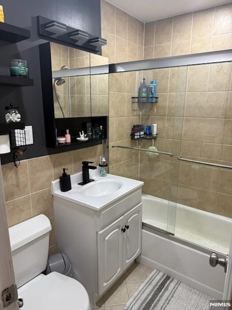 full bath with toilet, bath / shower combo with glass door, tile walls, and tile patterned floors