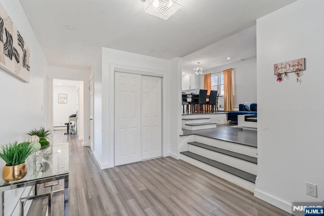 corridor with baseboards, wood finished floors, and a notable chandelier