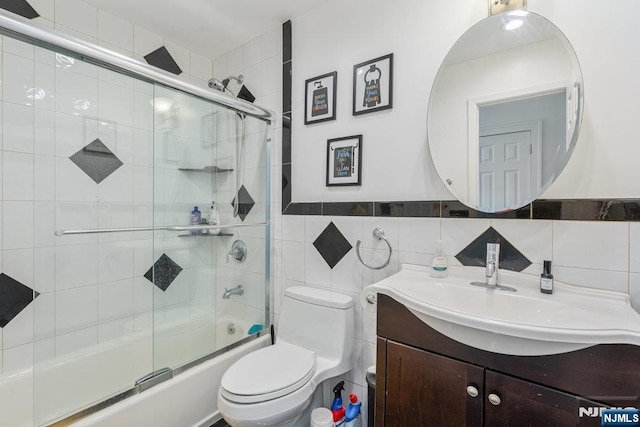 full bathroom with tile walls, vanity, toilet, and bath / shower combo with glass door