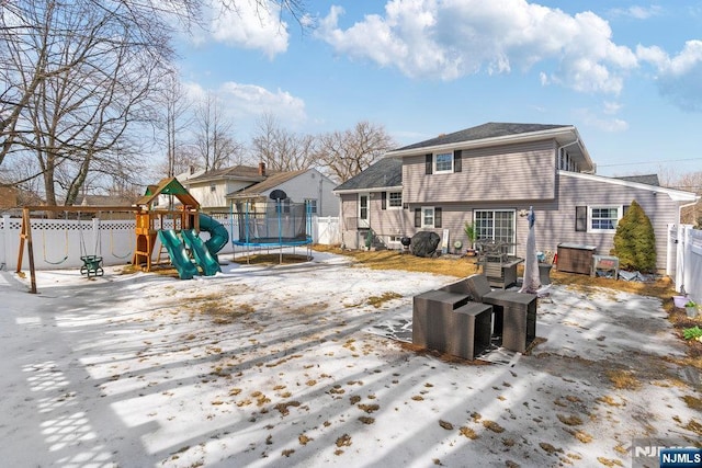 snow covered back of property with a trampoline, fence, and a playground