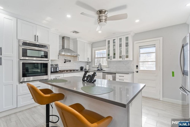 kitchen with visible vents, wall chimney exhaust hood, appliances with stainless steel finishes, a breakfast bar area, and backsplash