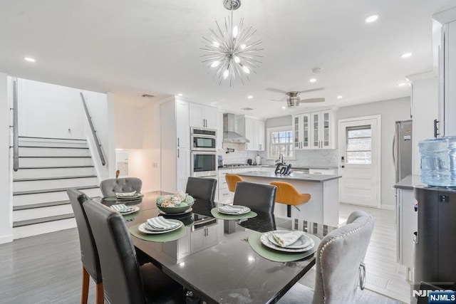 dining room with recessed lighting, baseboards, stairs, light wood-style floors, and ceiling fan with notable chandelier