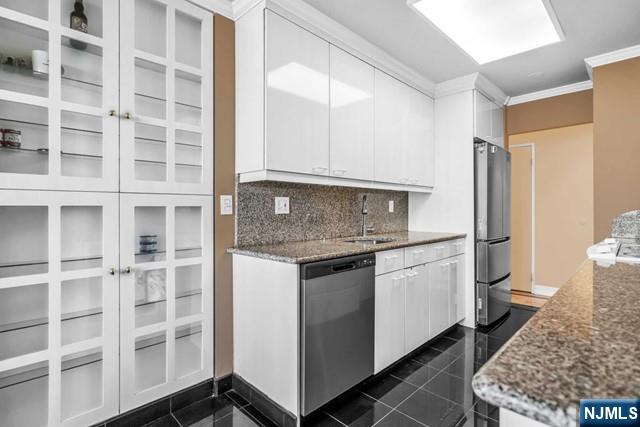 kitchen with stainless steel appliances, a sink, white cabinets, ornamental molding, and dark stone counters