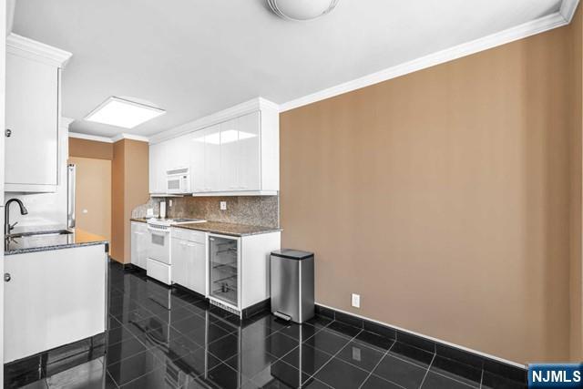 kitchen with wine cooler, white appliances, a sink, white cabinets, and ornamental molding