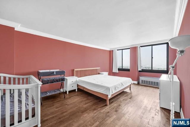 bedroom featuring ornamental molding, radiator heating unit, and wood finished floors