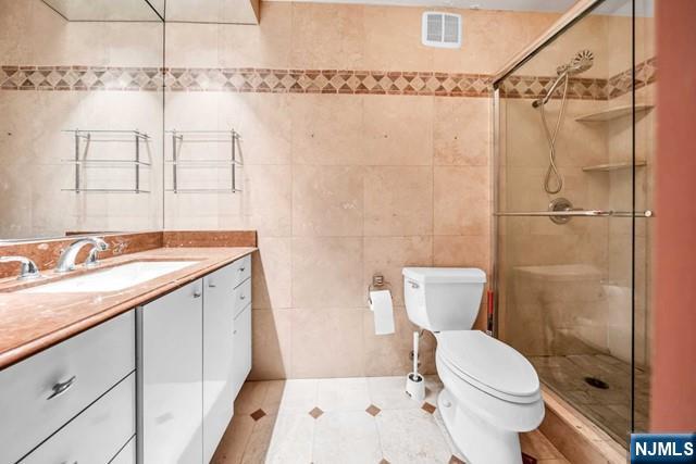 full bath featuring toilet, a stall shower, vanity, and visible vents