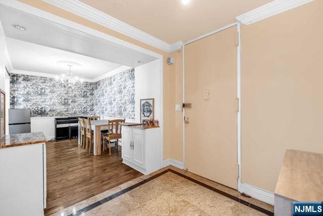 foyer entrance featuring a notable chandelier, crown molding, baseboards, and wallpapered walls