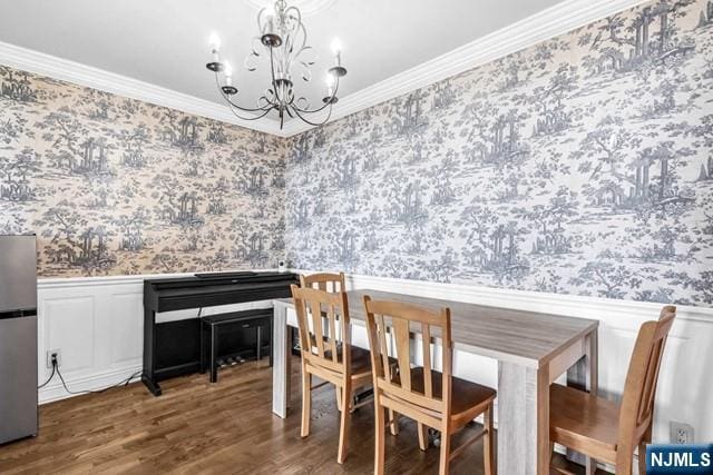 dining area with a wainscoted wall, an inviting chandelier, ornamental molding, wood finished floors, and wallpapered walls