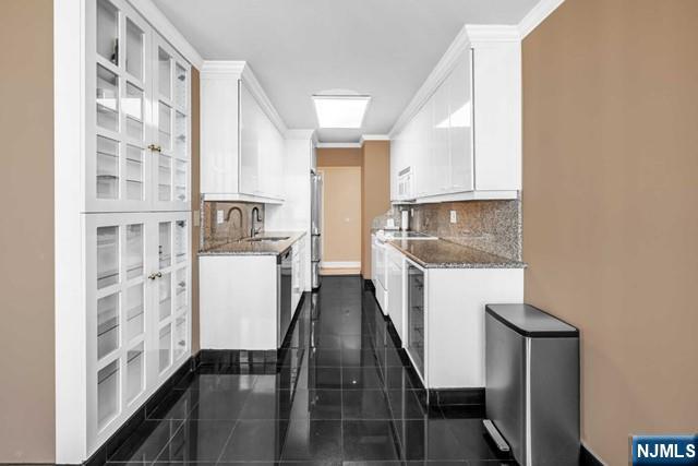 kitchen featuring dishwasher, ornamental molding, white cabinets, and a sink